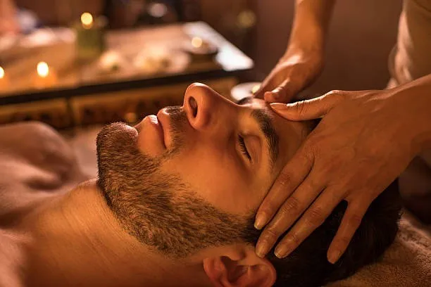 Massage des tempes d’un homme allongé, à la lueur des bougies