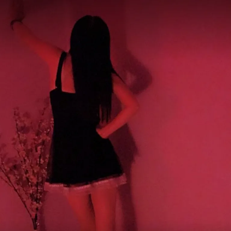 Une masseuse en robe noire, de dos, dans une lumière rose