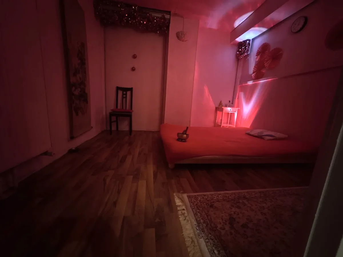 Salle de massage aux lumières rouges, avec un matelas, une chaise et un tapis